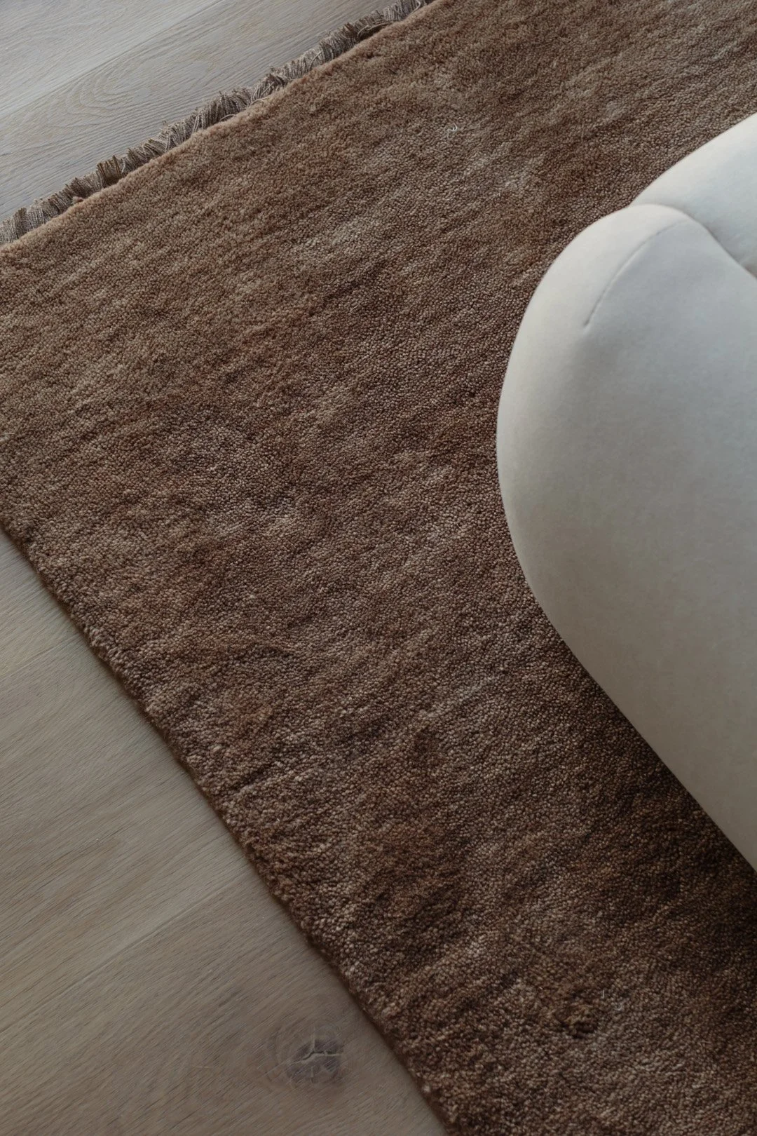 Close-up of a brown textured rug on light-colored wooden floor next to a piece of white furniture.