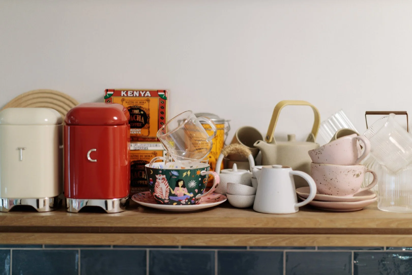 Collection of kitchenware including teapots, cups, glasses, boxes, and small bowls on a wooden shelf.