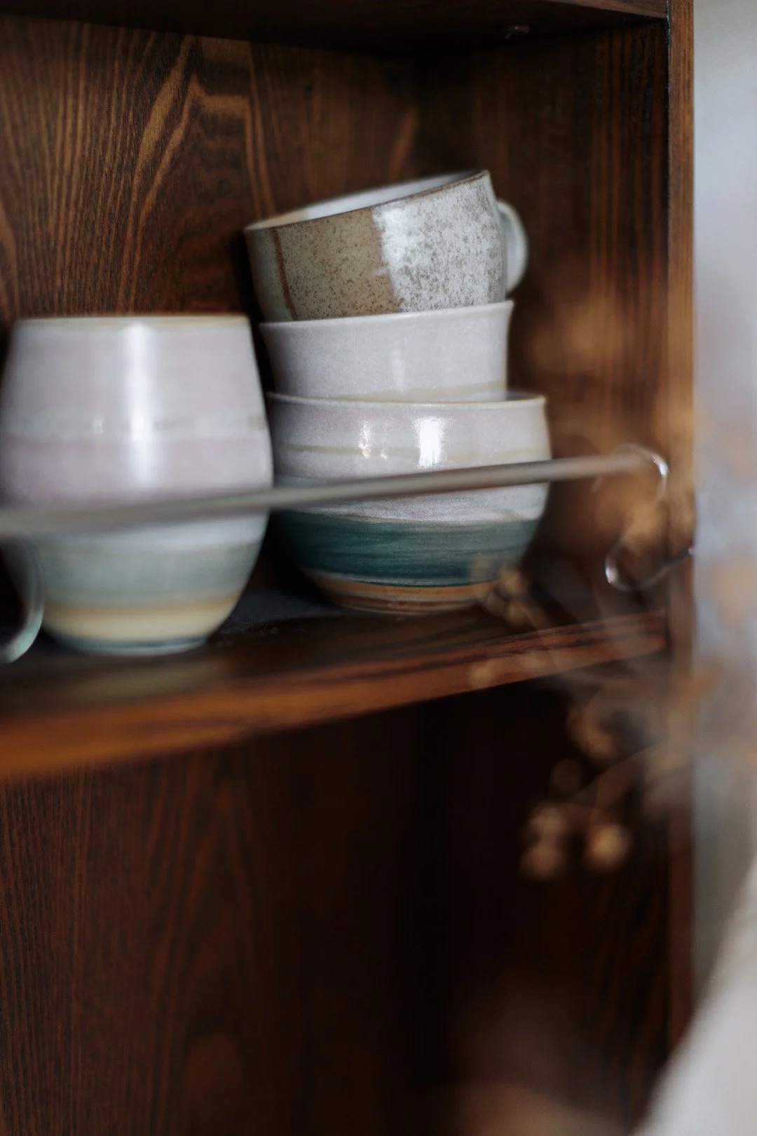 Stacked ceramic cups inside a wooden cabinet, with multiple layers of cups visible.
