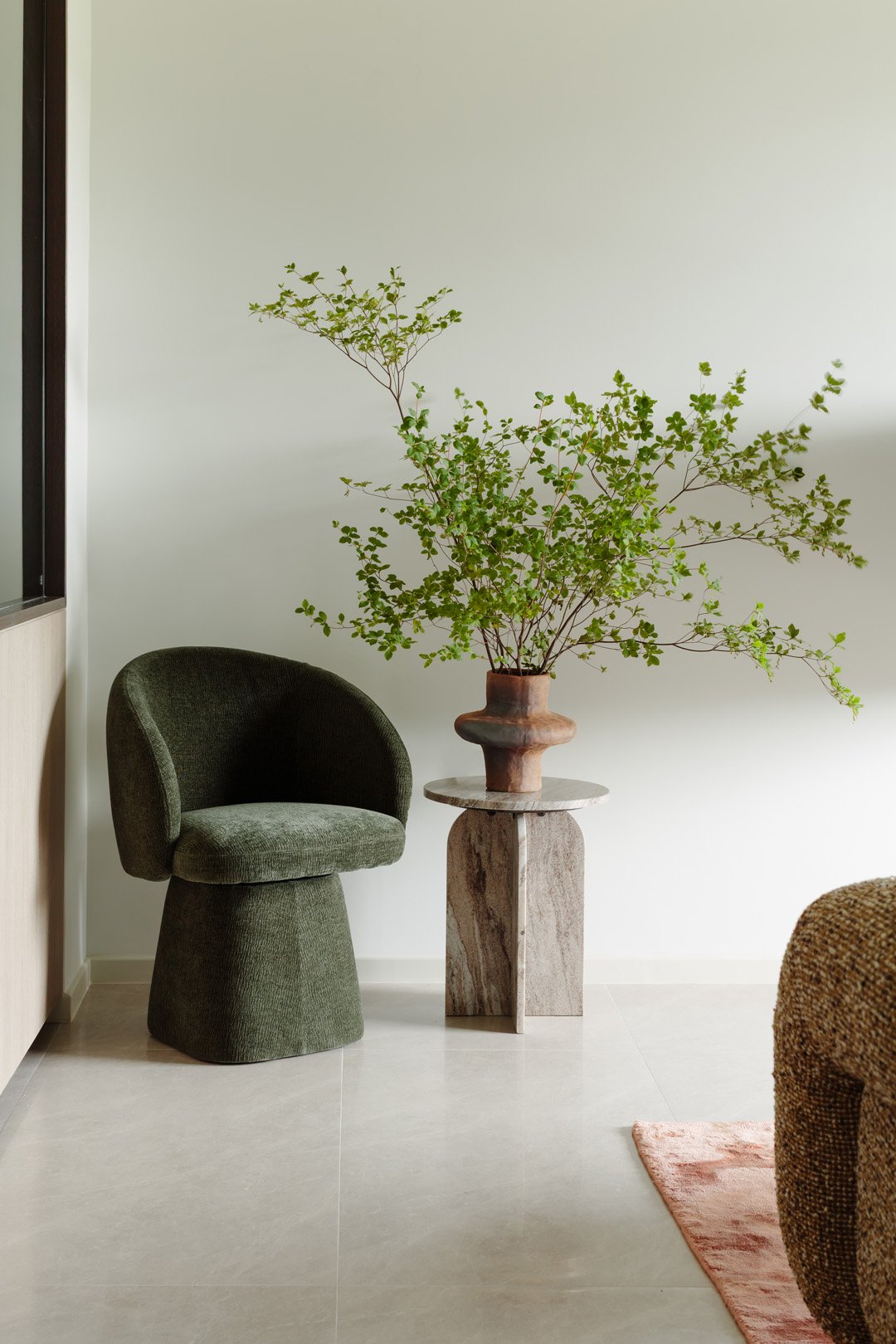 A green velvet chair and a wooden side table with a large green leafy plant in a decorative brown vase.