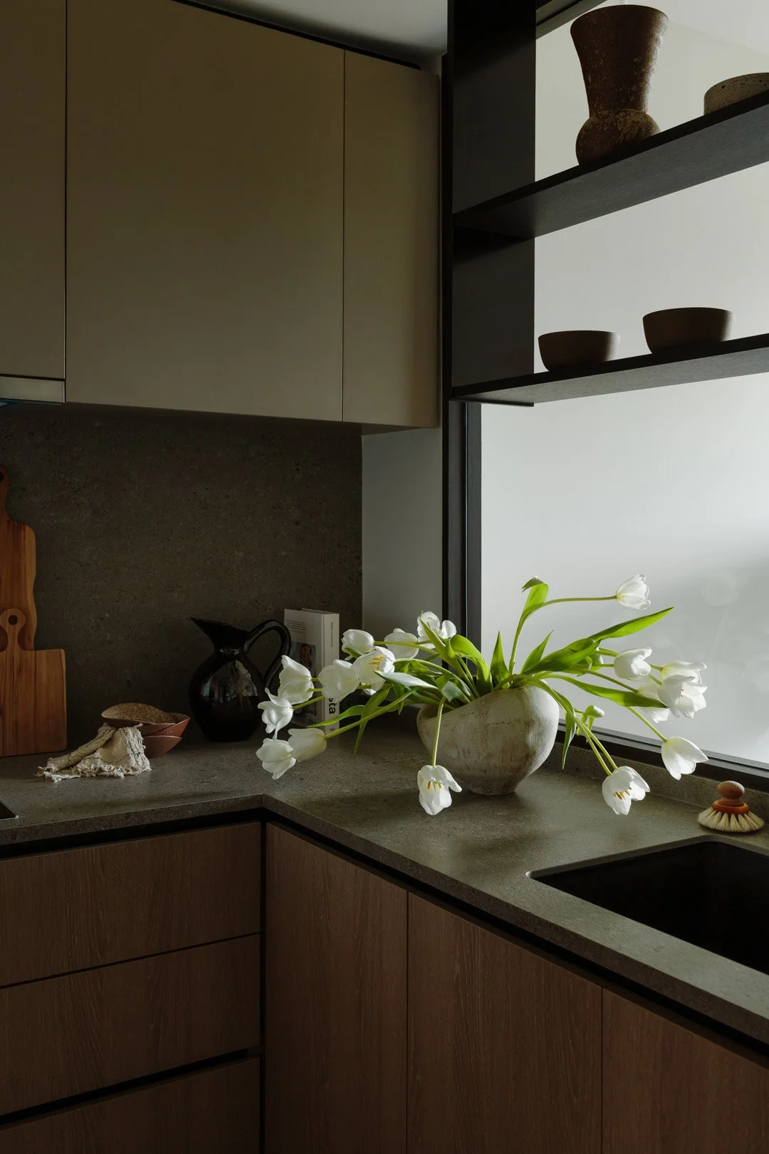 A kitchen countertop with a white vase holding white tulips, placed near a window.