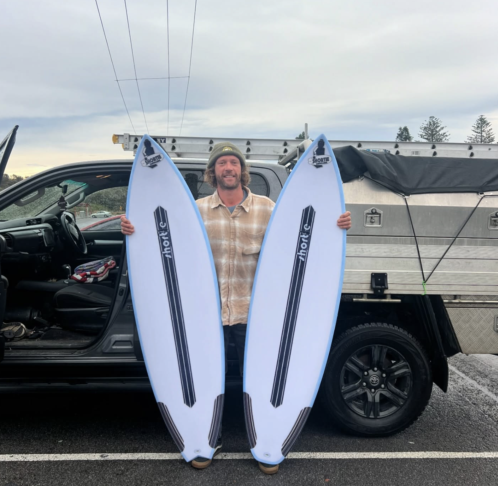 A happy customer holding brand new two white surfboards with carbon fibre stringers, ready for a surf trip to Indonesia.