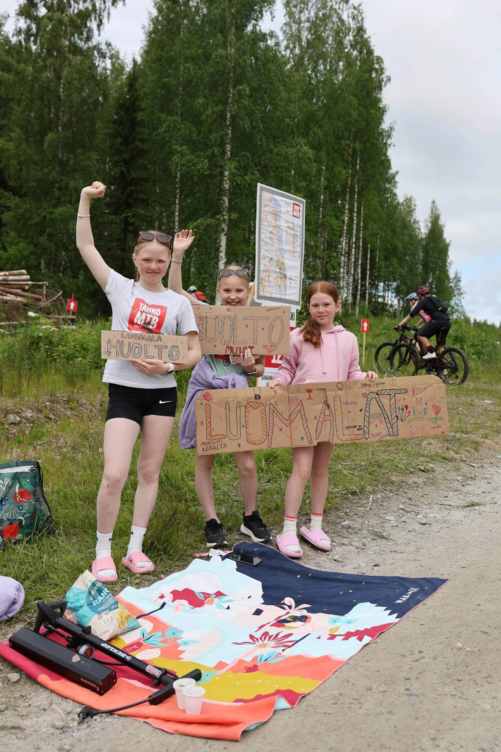 Kolme lasta seisoo luonnossa, pitäen käsissään kylttejä, joihin on kirjoitettu käsin esim. "Huolto".