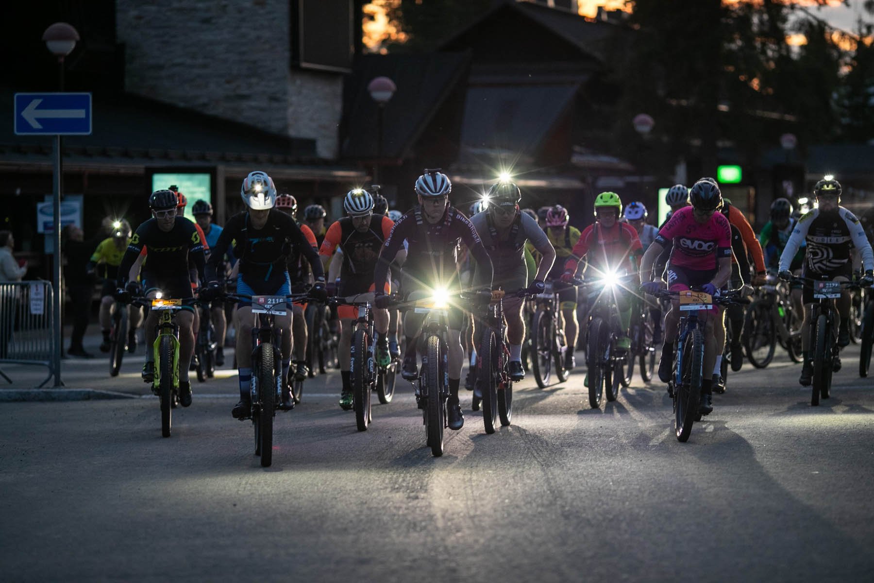 Maastopyöräilijöitä ajaa pimeässä, he kilpailevat ja heillä on pyöräilyvarusteet ja pyörissä valot.