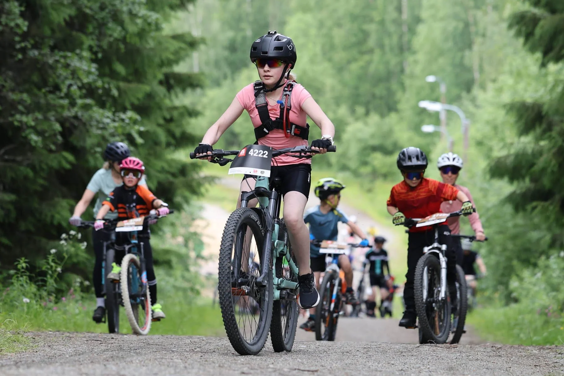 Lapsia pyöräilemässä metsässä pyöräilykilpailussa, heillä kypärät ja pyöräilyvarusteet.