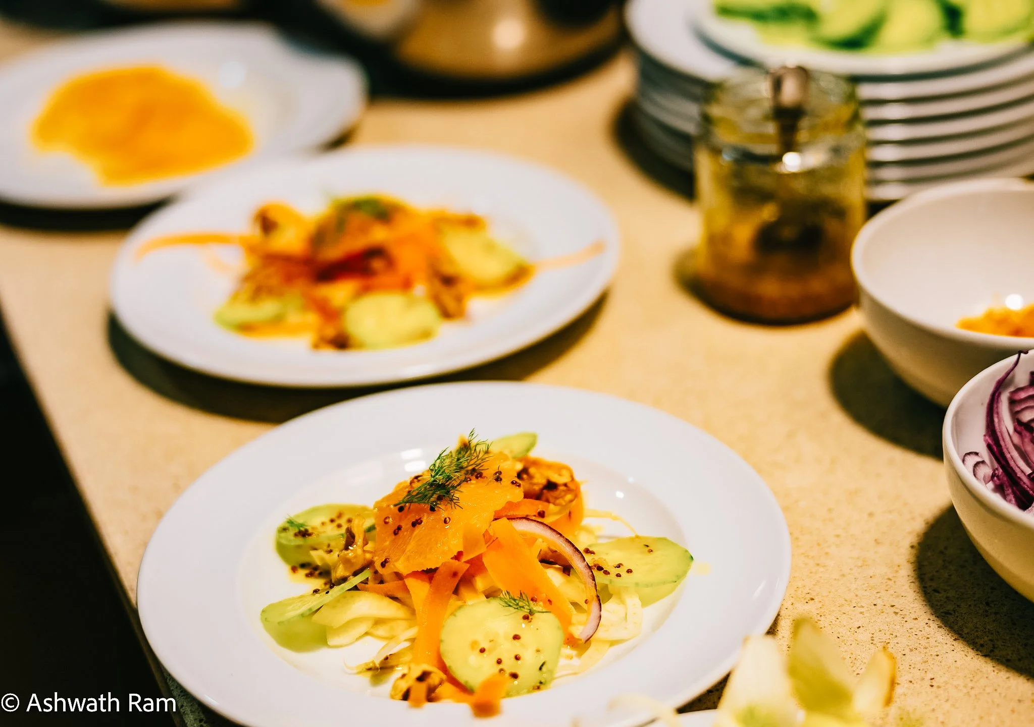 Close-up of a plated salad with thinly sliced cucumbers, shredded carrots, red onions, and garnished with dill and mustard seeds on a white dish.
