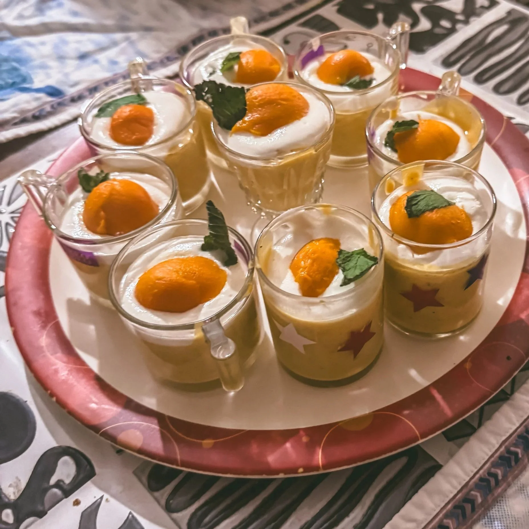 Tray of small glasses filled with a dessert topped with orange slices and mint leaves, placed on a stove.