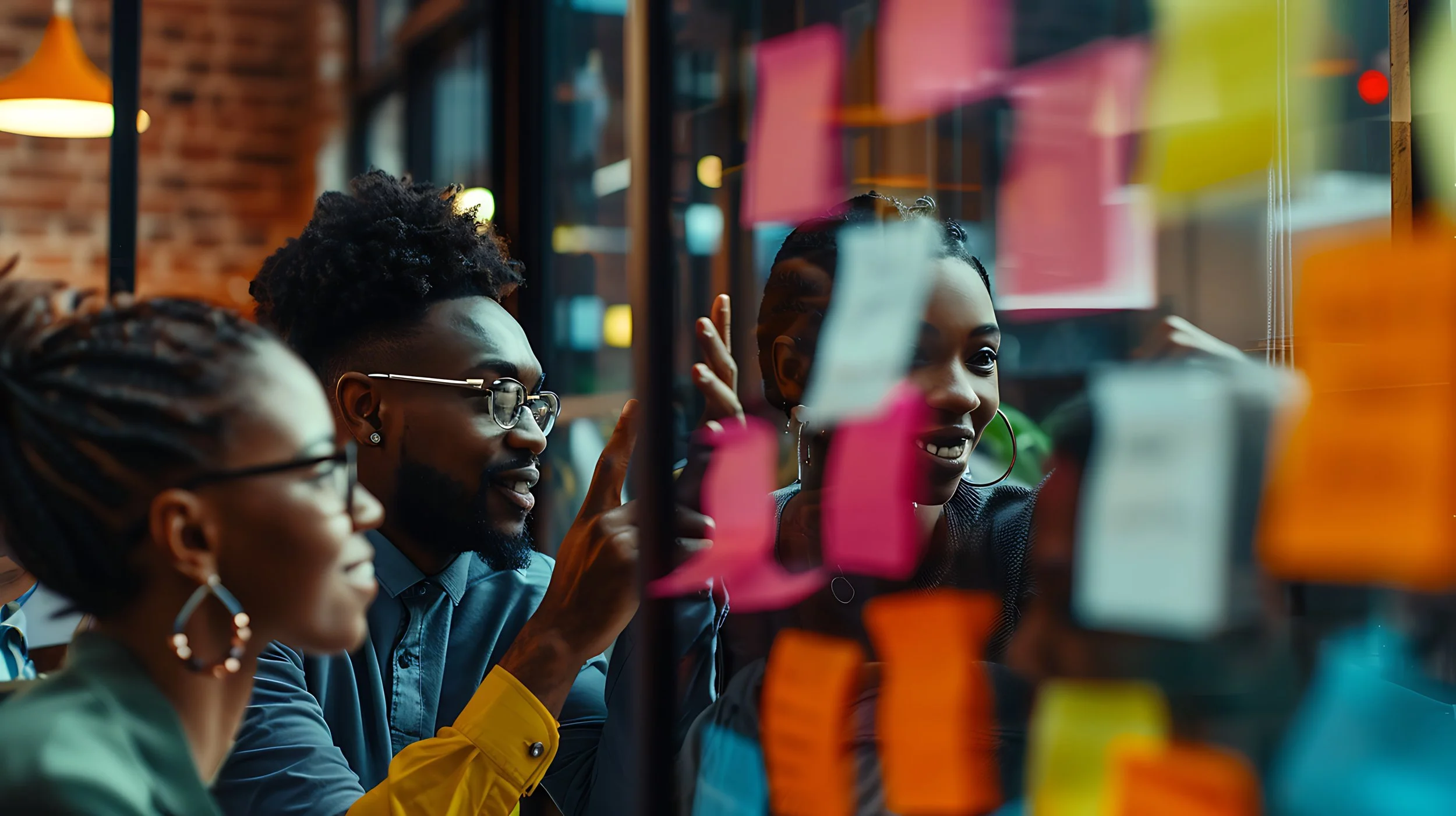 Group of diverse people smiling and writing on sticky notes on a glass wall in a modern office.