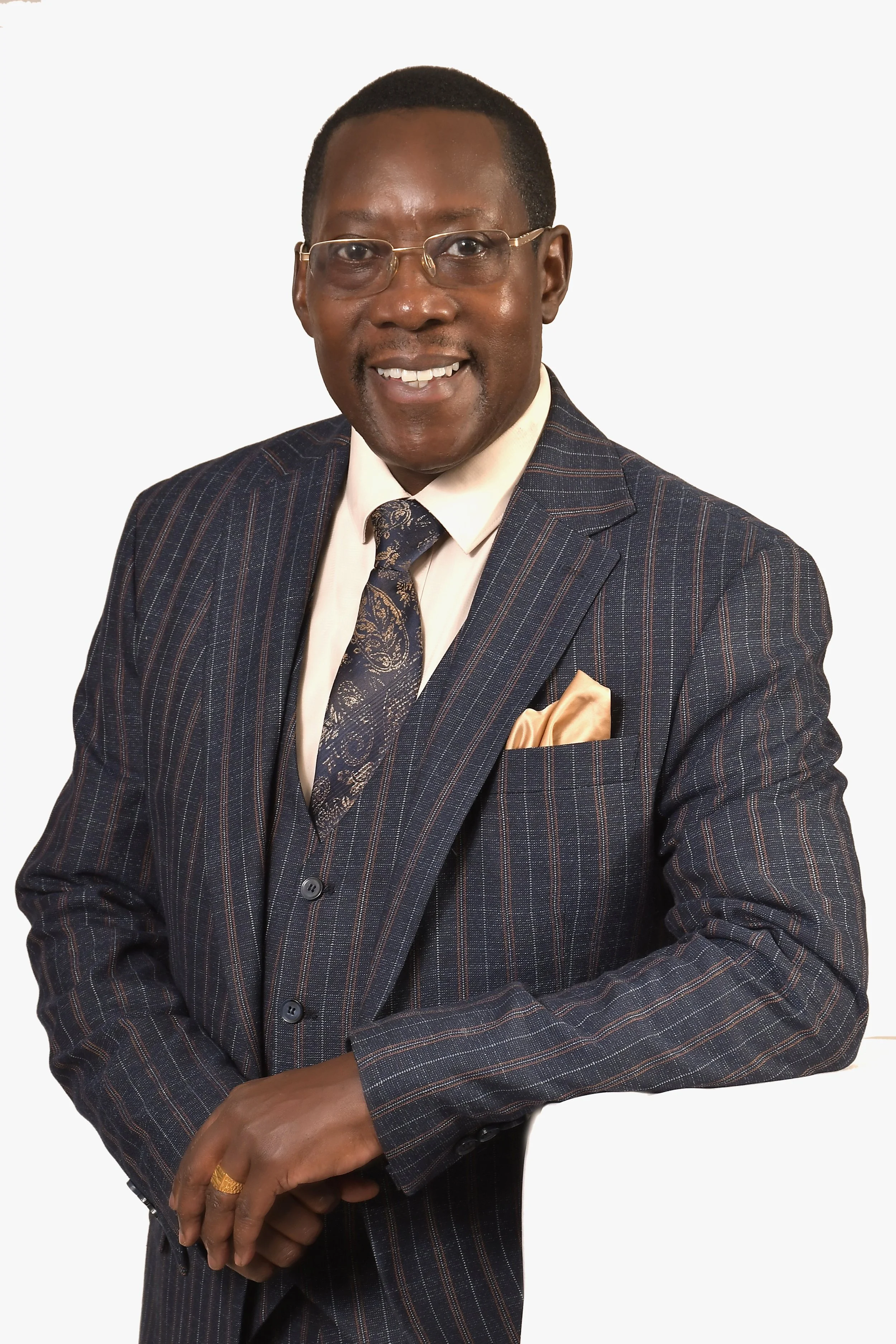 A man wearing glasses, a dark pinstripe suit with a tie, and a light-colored pocket square, smiling with arms crossed against a plain white background.