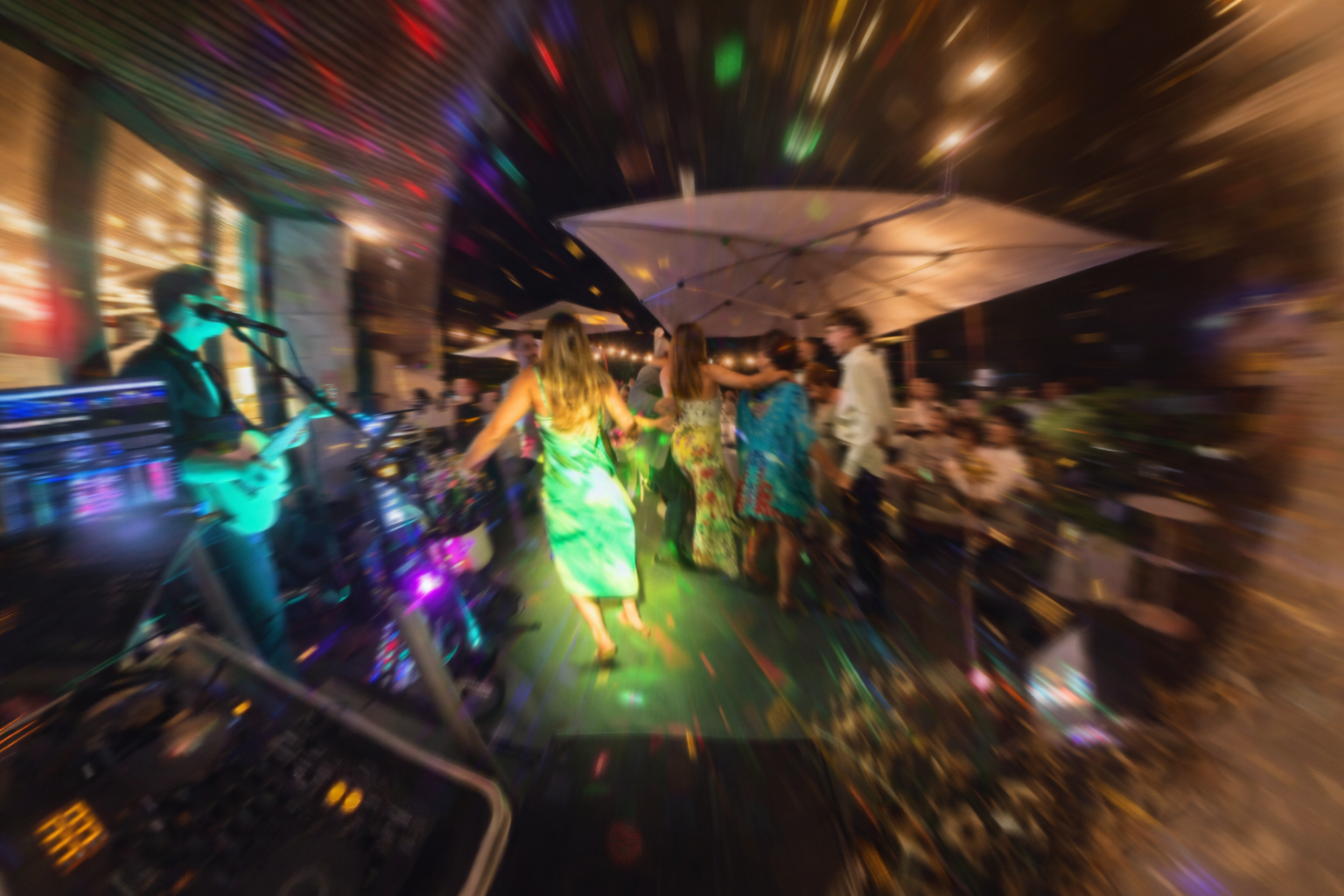 People dancing under a tent at a lively outdoor party with James from Hearts Afire playing guitar on stage, colourful lights, and a crowd of guests in and out of focus.
