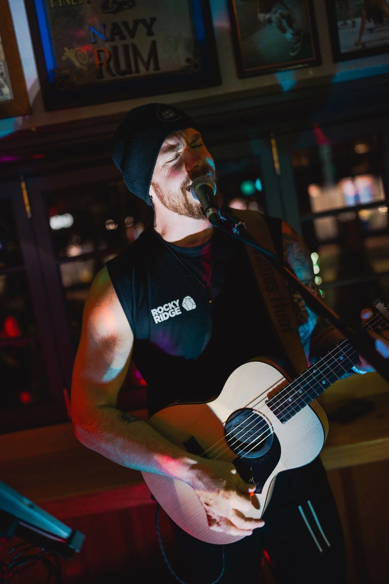 James Hunt from Hearts Afire is singing into a microphone while playing an acoustic guitar in a bar or pub setting.