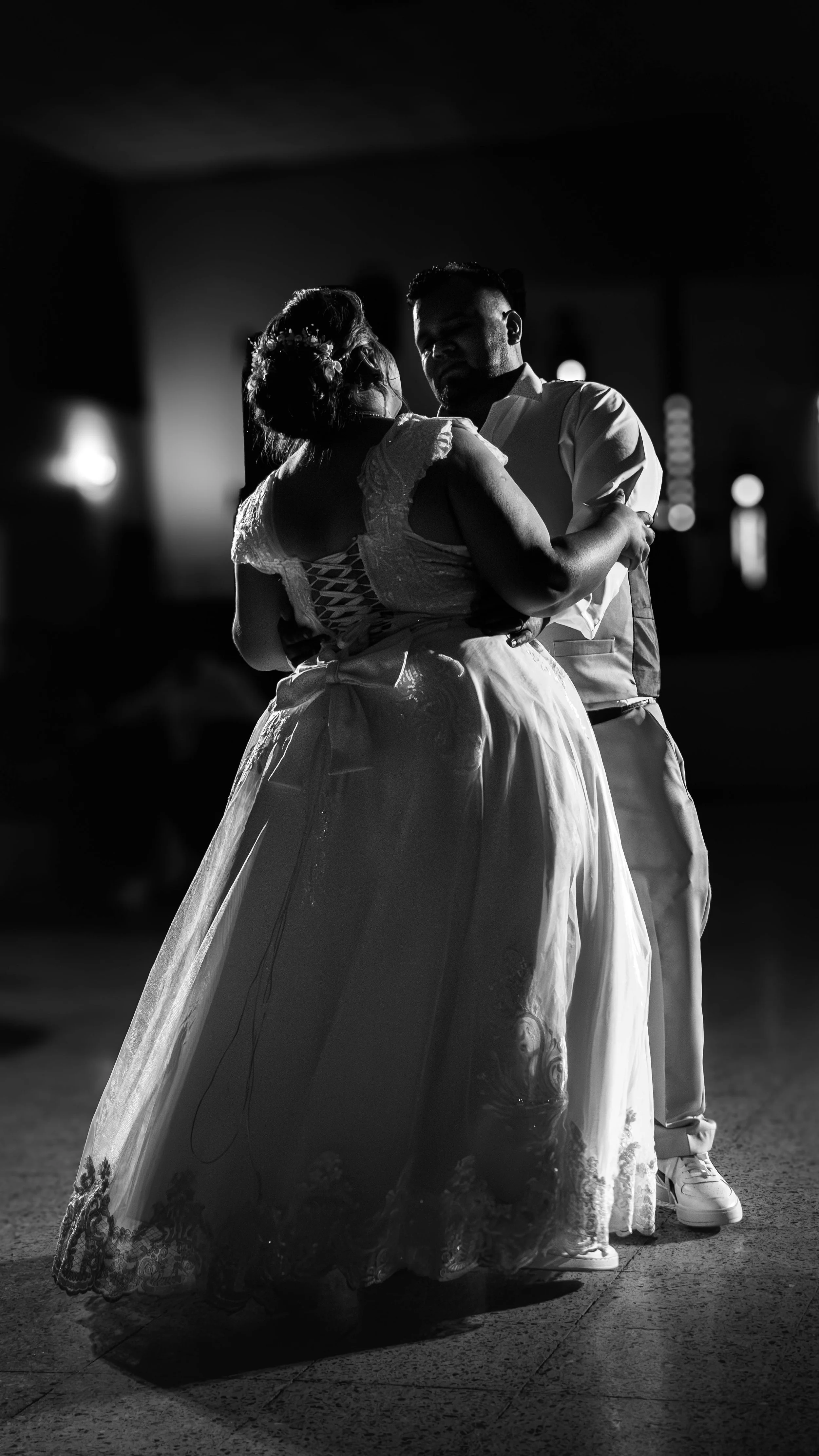 A couple dancing closely during a nighttime event, illuminated by soft lighting, in black and white.