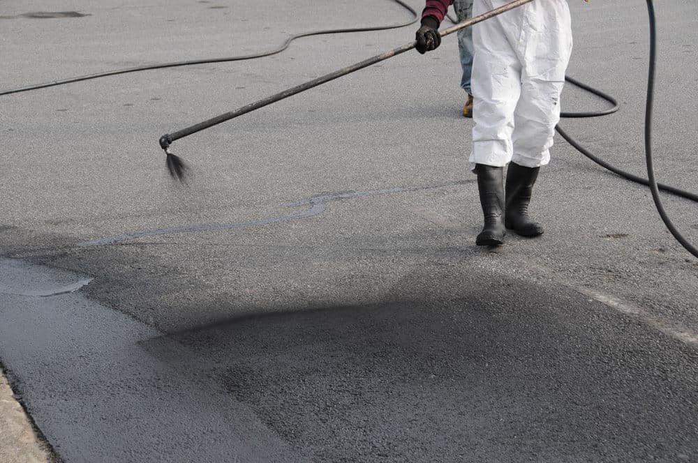 Worker in white protective suit and black boots applying asphalt with a long pole