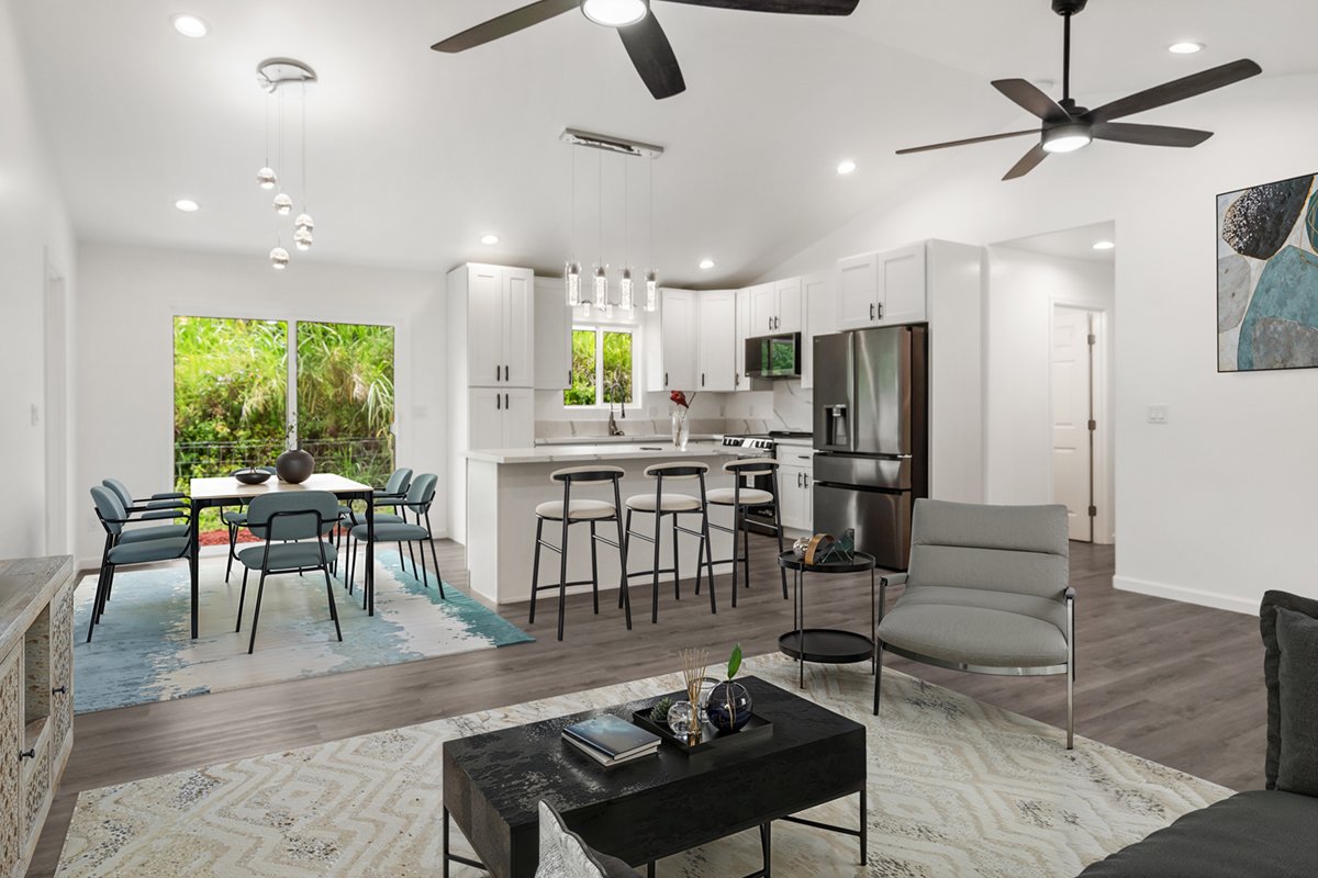 Open-concept living area with kitchen, dining space, and seating. White cabinets, stainless steel appliances, dark wood floors, ceiling fans, large window, and abstract art.