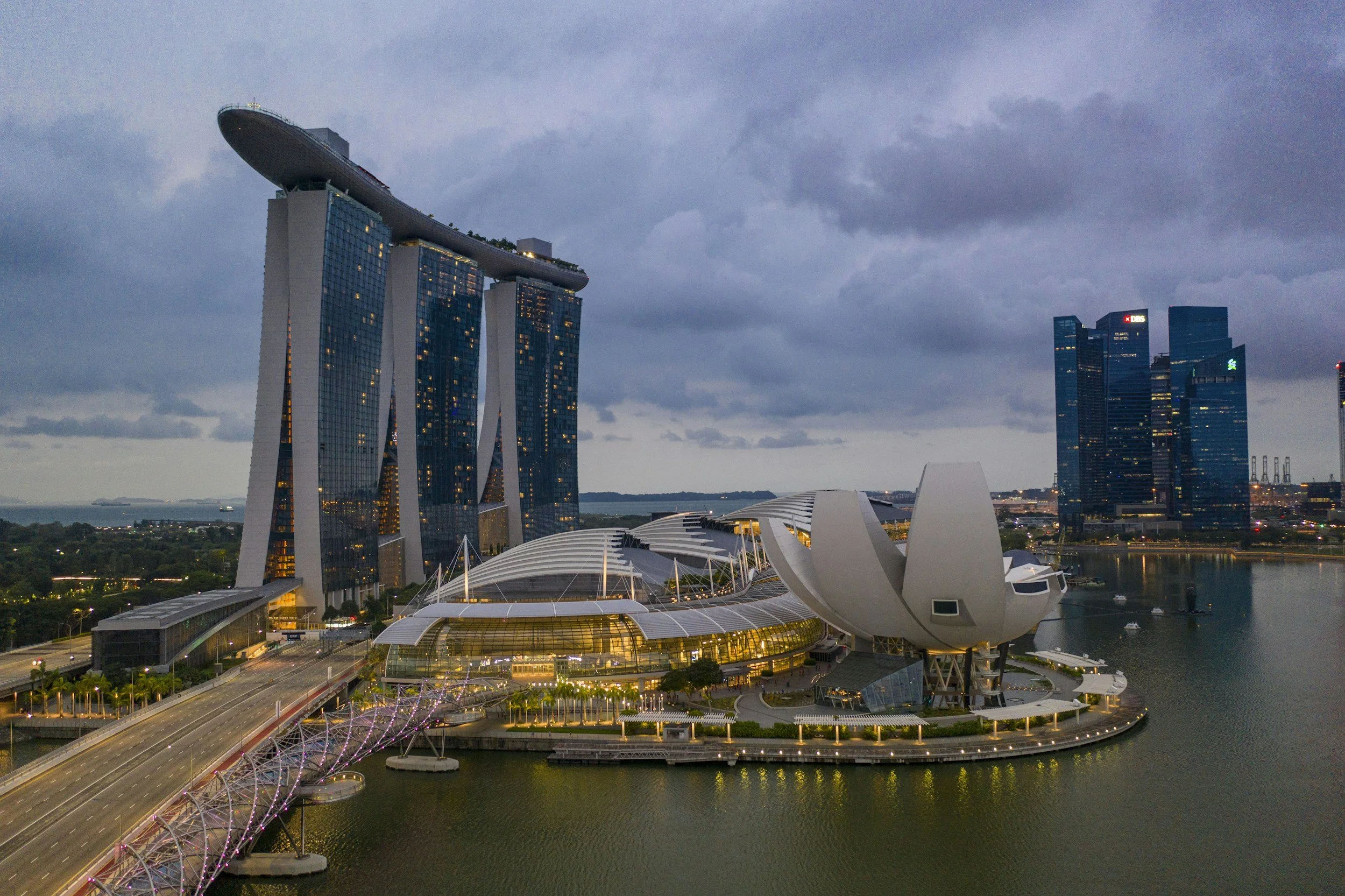 Nighttime view of Marina Bay Sands hotel with its three towers and boat-shaped roof, the ArtScience Museum in front, and other high-rise buildings across the bay in Singapore.