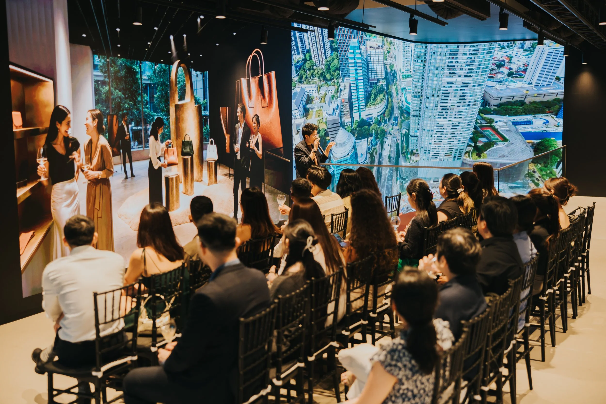 People at a wine tasting event with wine bottles on tables, in a modern venue with large windows and dark ceiling.