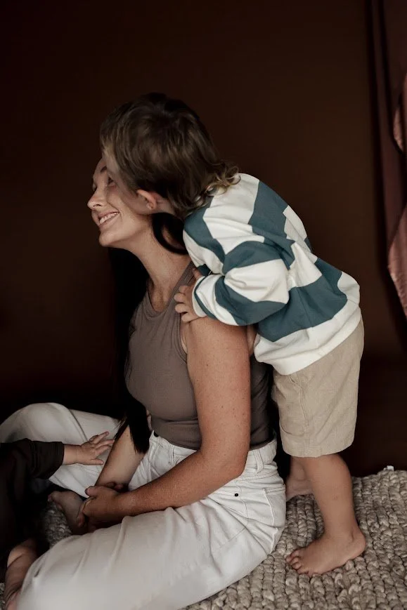 A woman with long dark hair smiling as a young boy, wearing a striped shirt, gives her a kiss on the cheek while sitting on her lap on a cozy blanket.