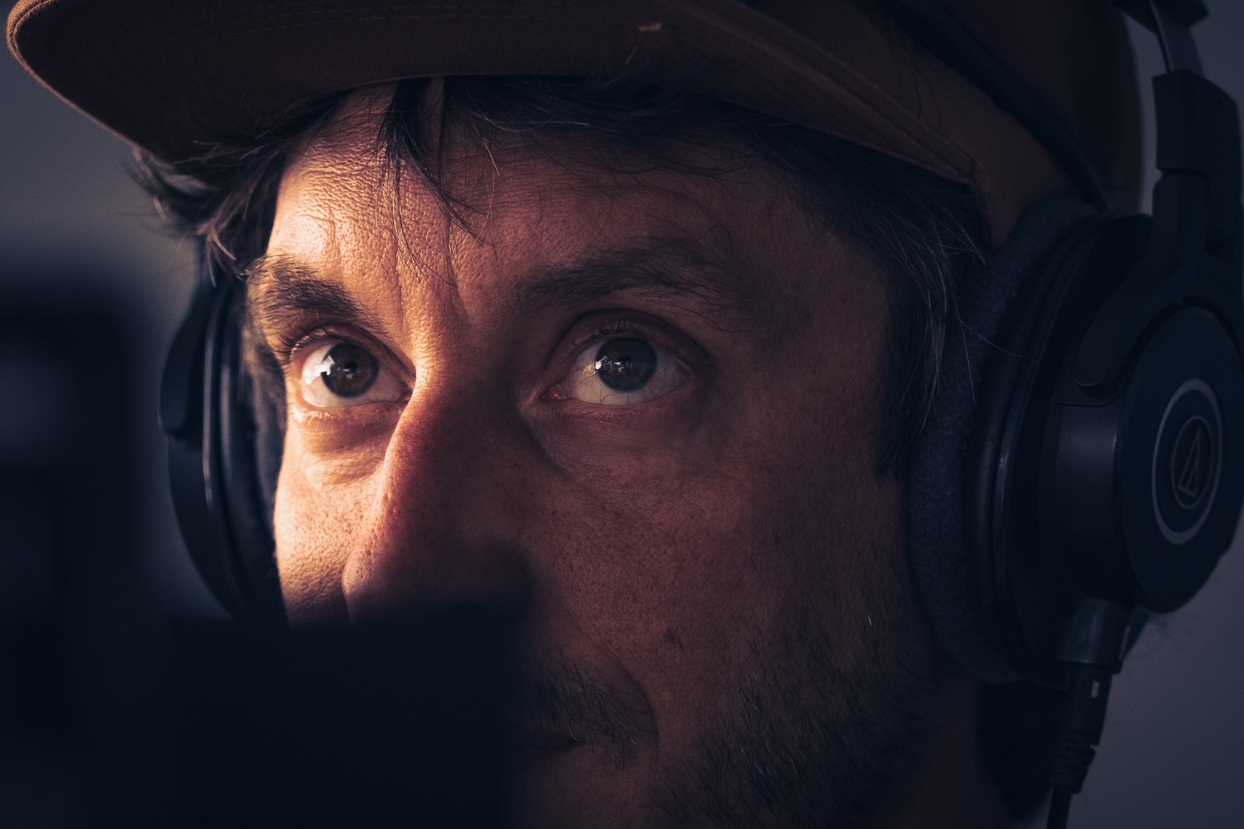 Close-up of a man wearing headphones and a hat, looking intently at something close in front of him.