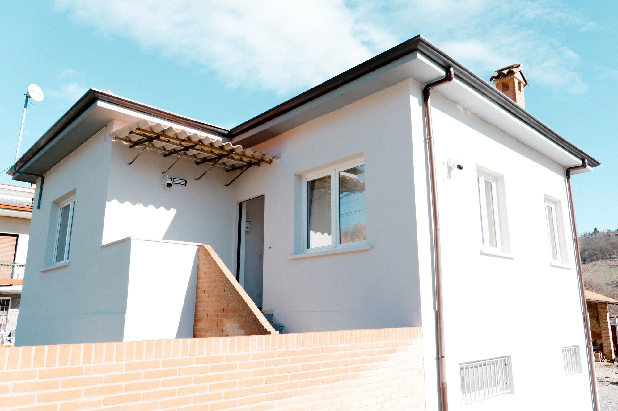 Casa moderna con pareti bianche, finestre grandi, tetto con tegole e un muro in mattoni.