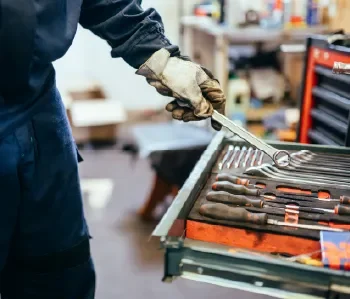 A person wearing gloves handling some tools in a toolbox in a workshop.