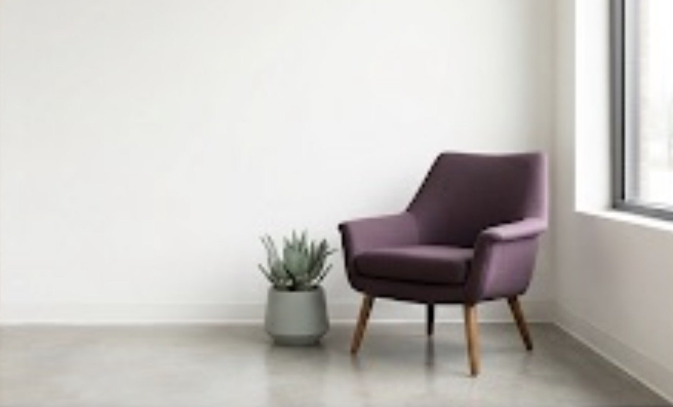 A purple armchair next to a potted plant, with a window on the right side in a minimalistic room.