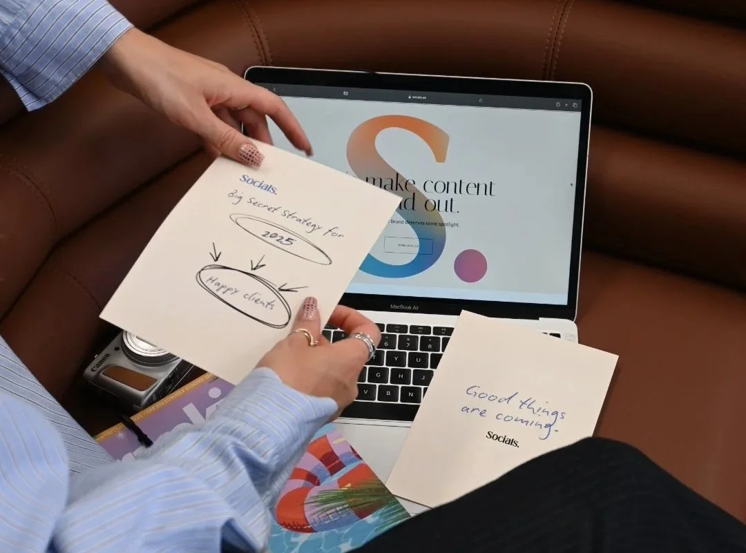 Person holding notes with handwritten ideas and messages in front of a laptop displaying a website about making content and strategizing for social media.