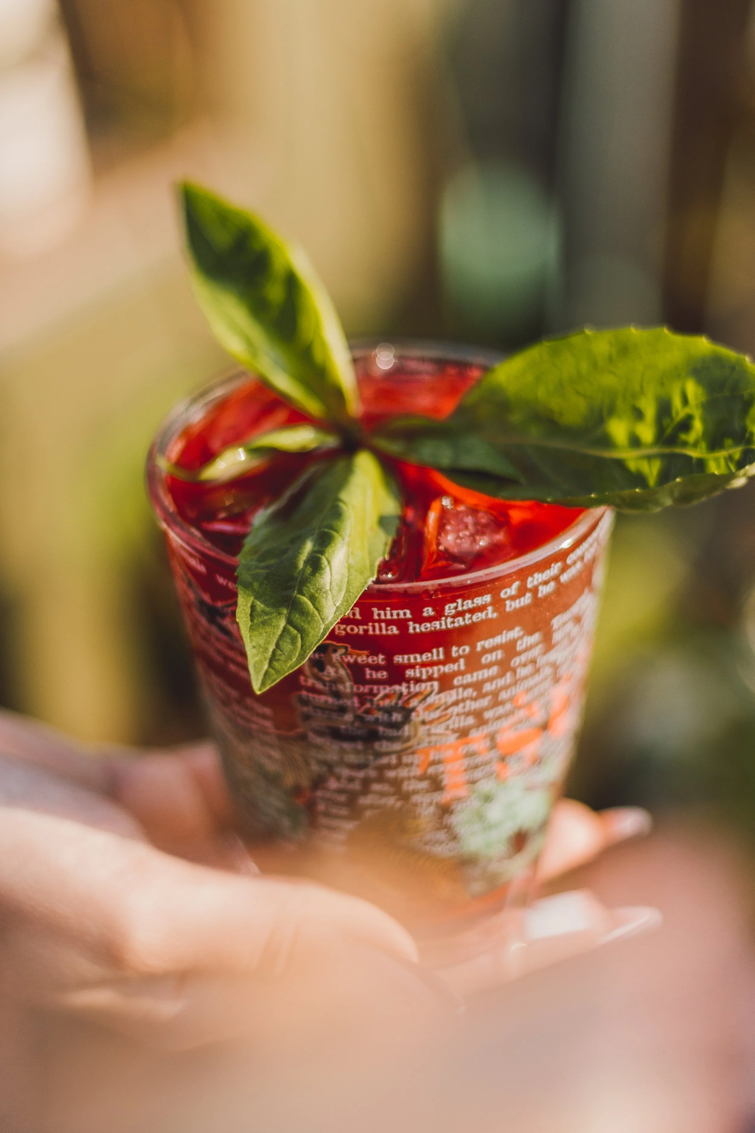 A glass containing a red beverage with ice and fresh green basil leaves on top.