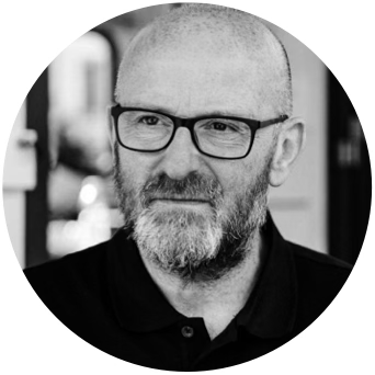 A black-and-white photo of a middle-aged man with glasses, a beard, and a shaved head, wearing a collared shirt.