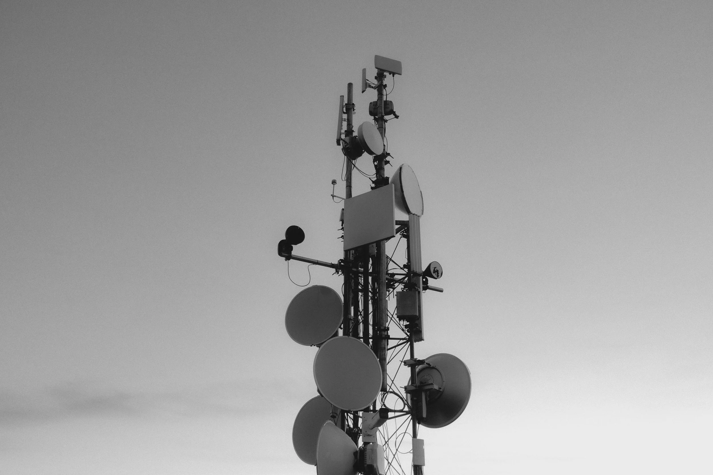 A tall communication tower with multiple satellite dishes and antennas mounted on it against a clear sky.