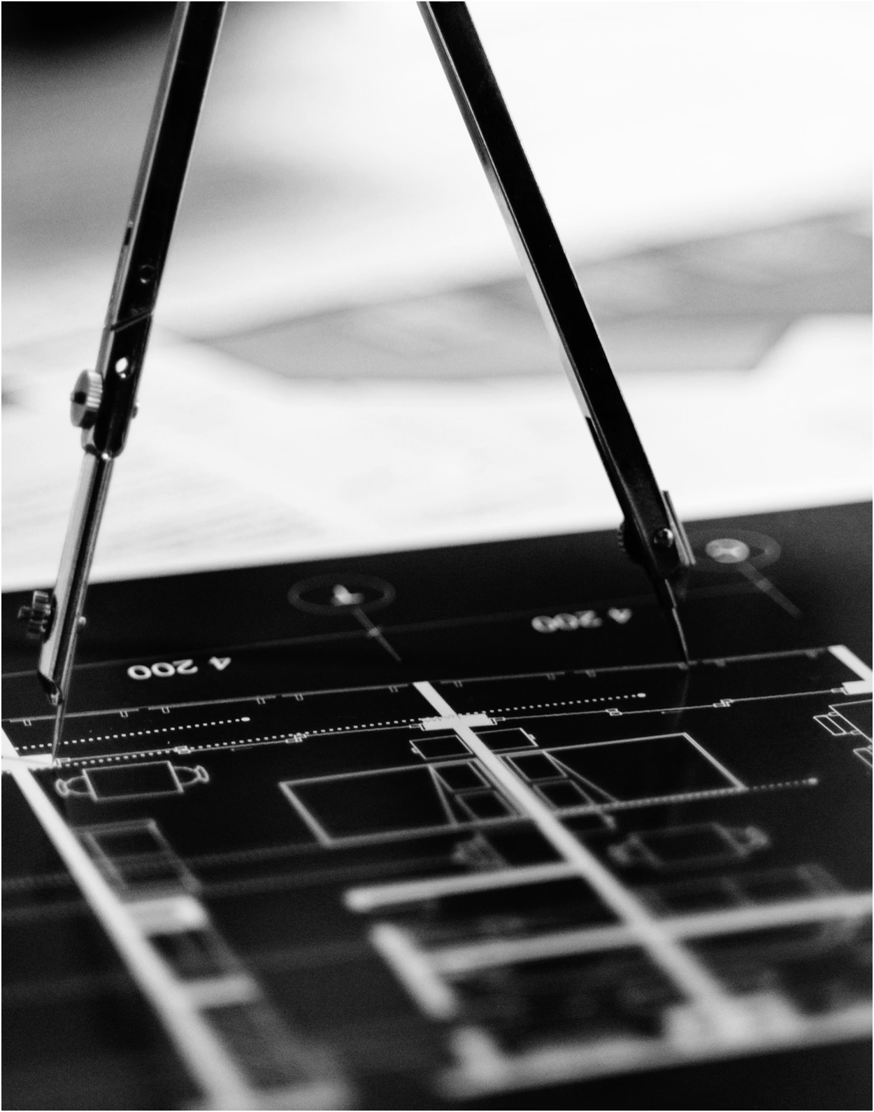 Close-up of a technical drawing on a blueprint with a pair of drafting compasses positioned over it.