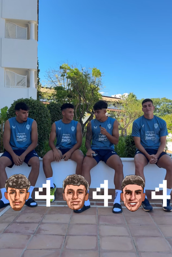 Cuatro jóvenes sentados en una banca, vistiendo uniformes deportivos azules, con figuras pixeladas de cabezas pretendiendo ser sus rostros en primera plano en el suelo delante de ellos, en un ambiente al aire libre con árboles y un edificio en el fondo.