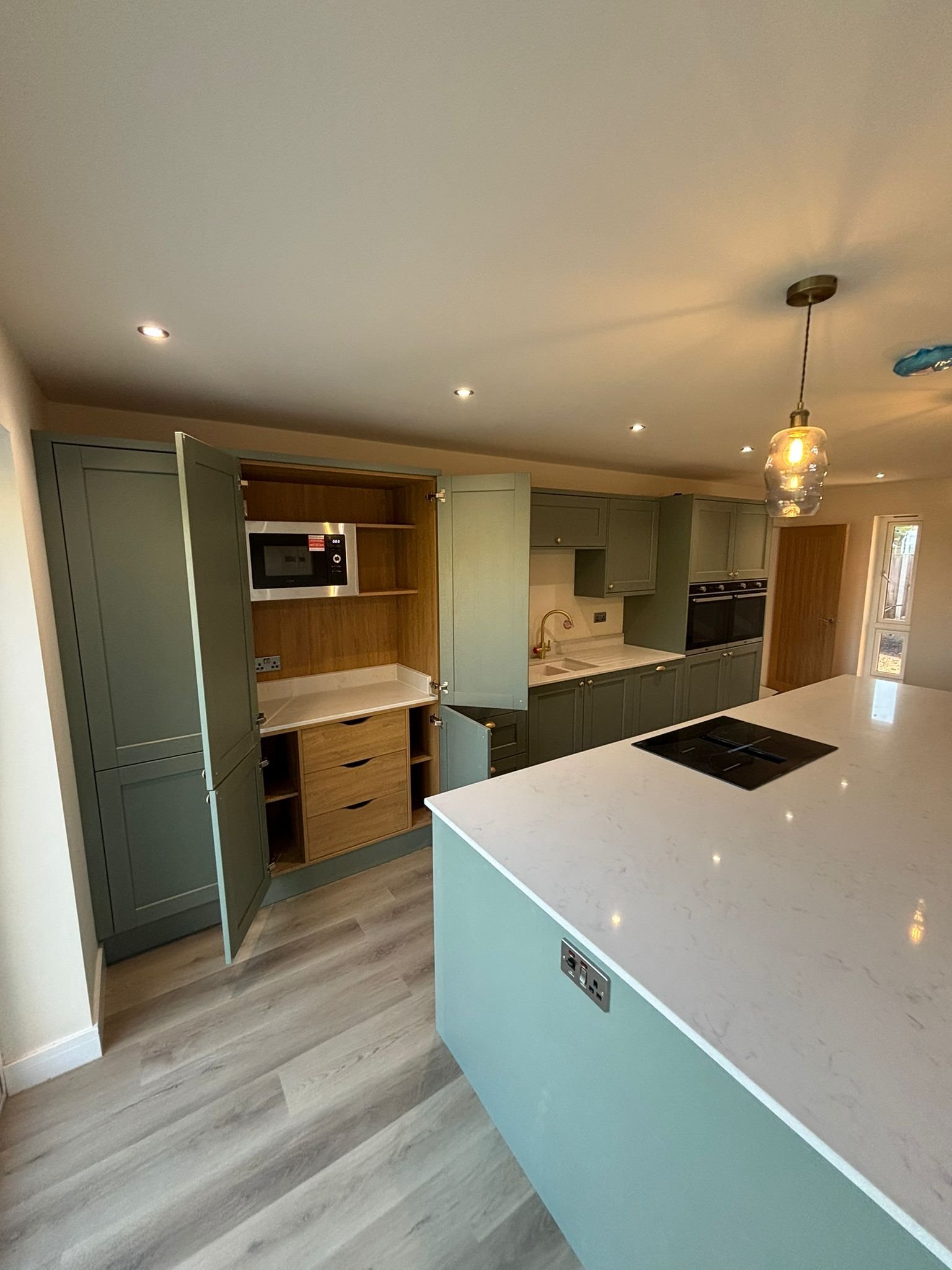 Modern kitchen with green cabinets, white marble island with electrical outlets, and a ceiling light fixture.