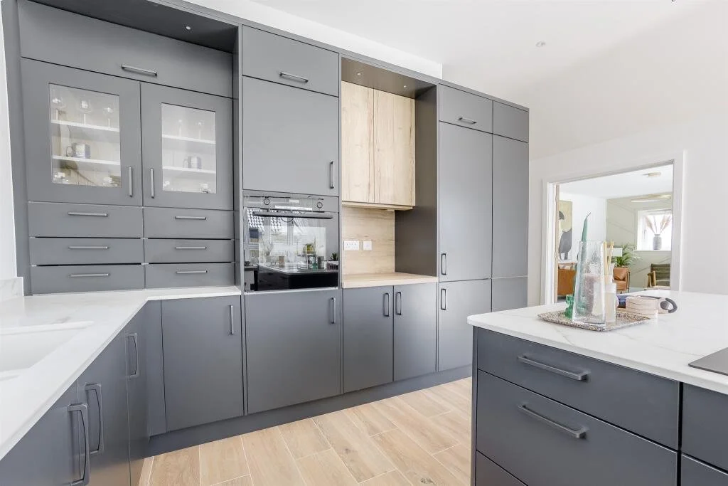 Modern kitchen with grey cabinets, built-in oven, and a white countertop island.