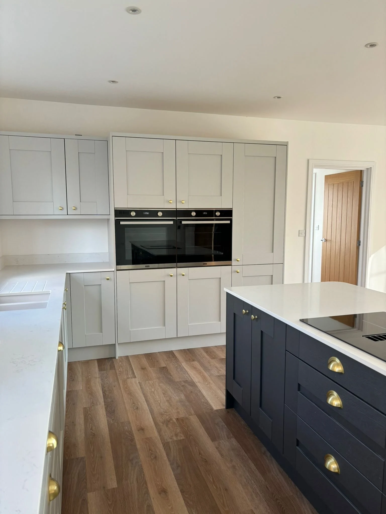 Bright kitchen with white and navy blue cabinets, wooden floor, and a wooden door to the right.