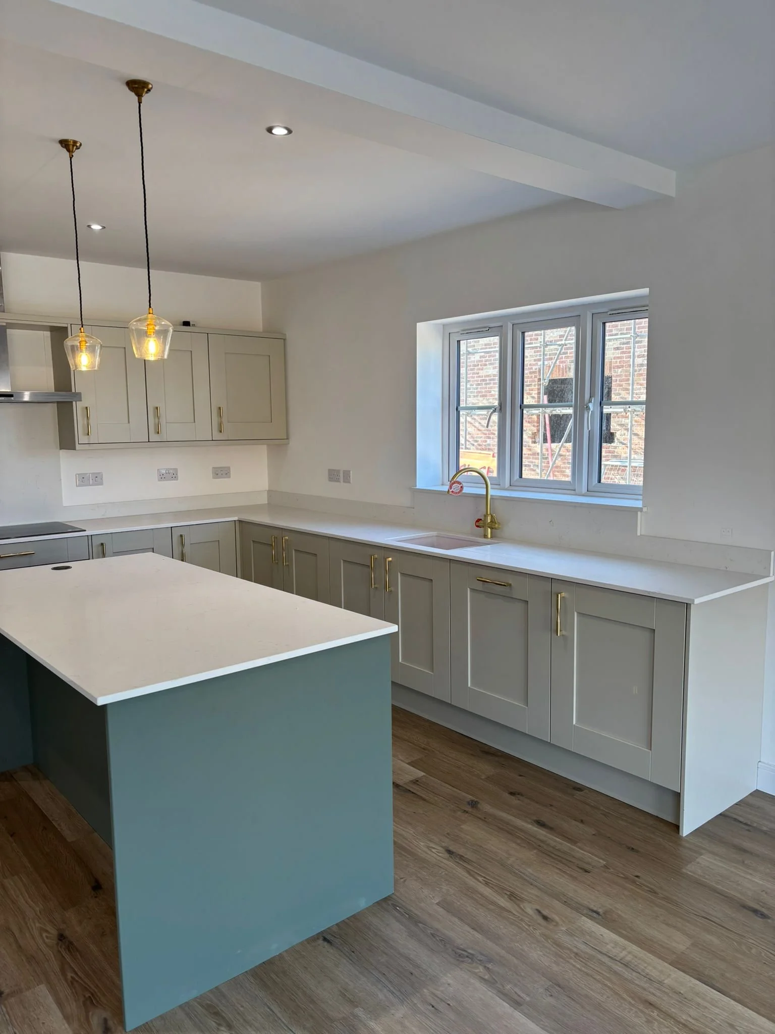 Modern kitchen with porcelain cabinets, white countertops, a window with a brick wall outside, and a reed green kitchen island.