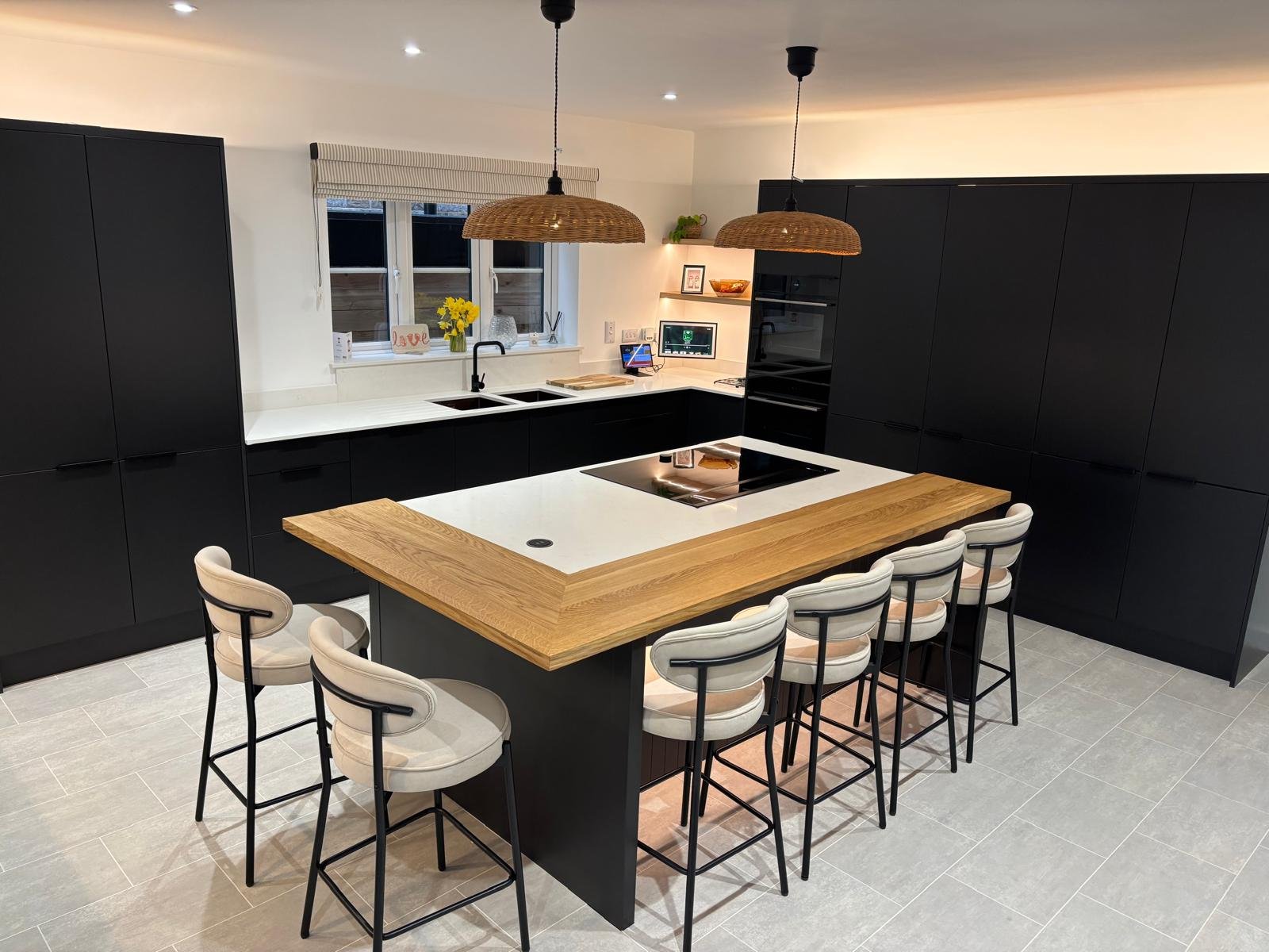 Modern kitchen with black cabinets, white countertops, wooden island with bar stools, two pendant lights, a window with a window sill, and a built-in oven and microwave.