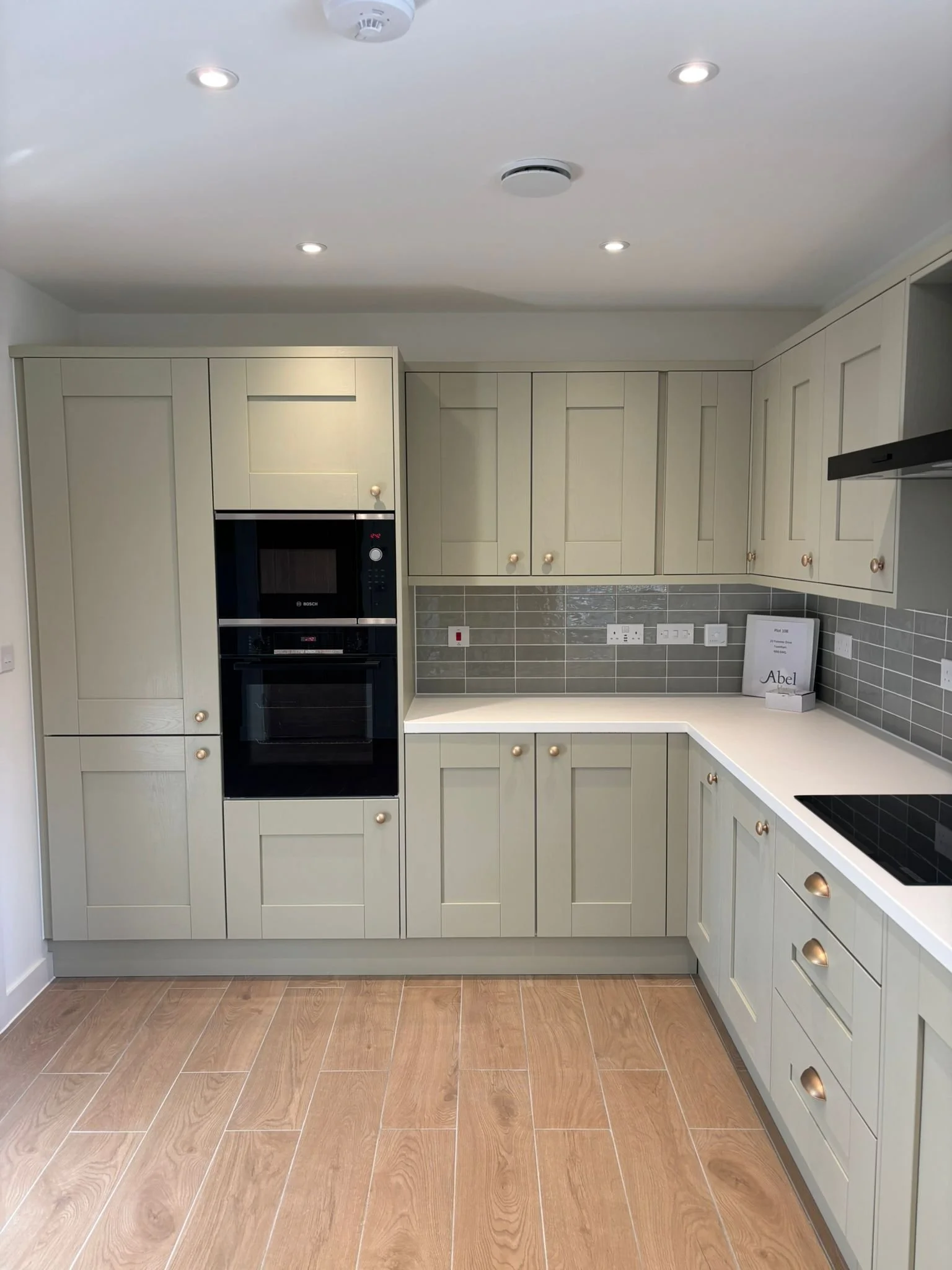 Modern kitchen with cream-colored cabinets, gray tile backsplash, built-in black microwave oven, and wooden floor.