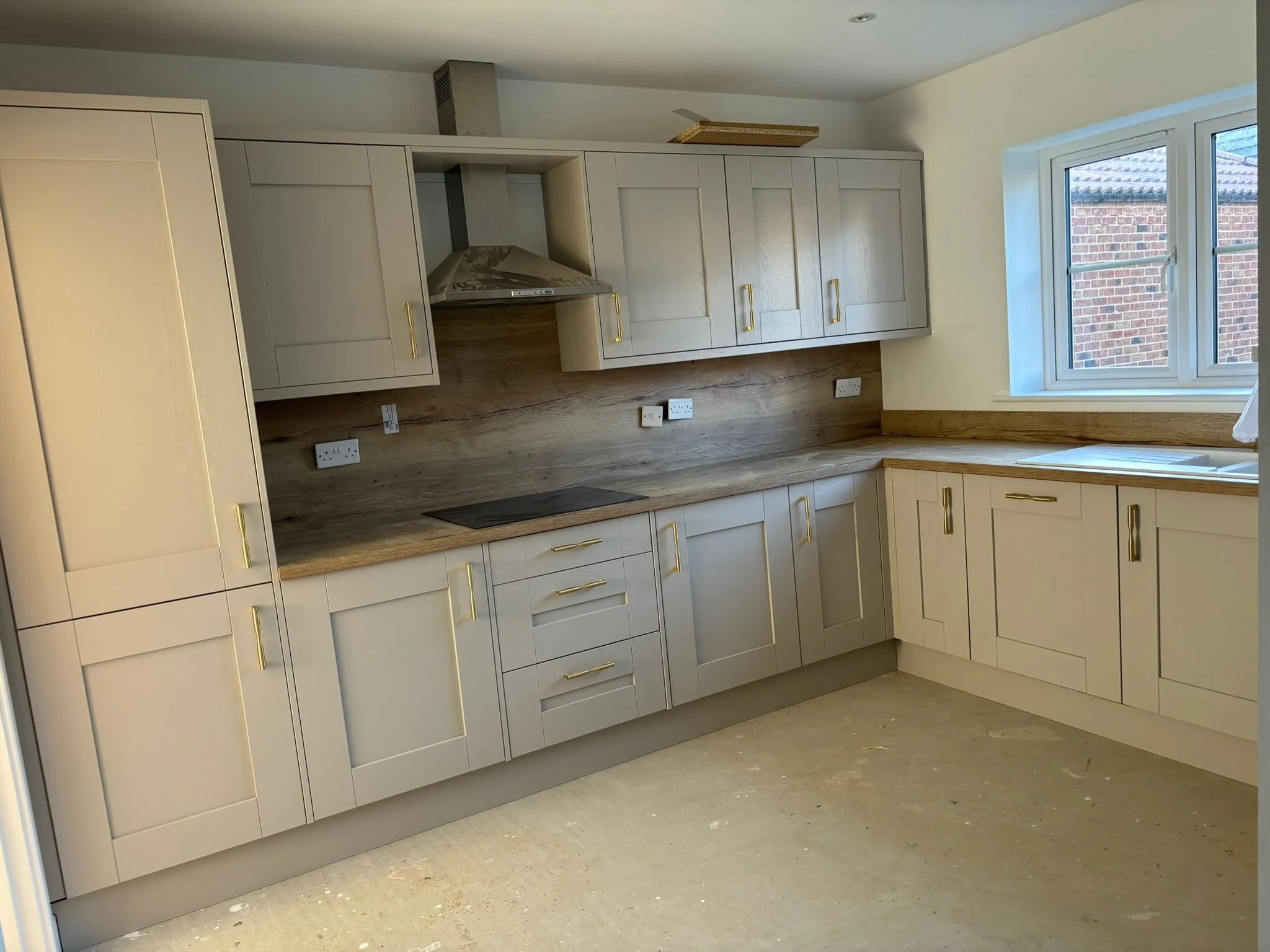 Kitchen with white cabinets, gold handles, wooden countertop, a window showing brick wall outside, and power outlets on the wall.