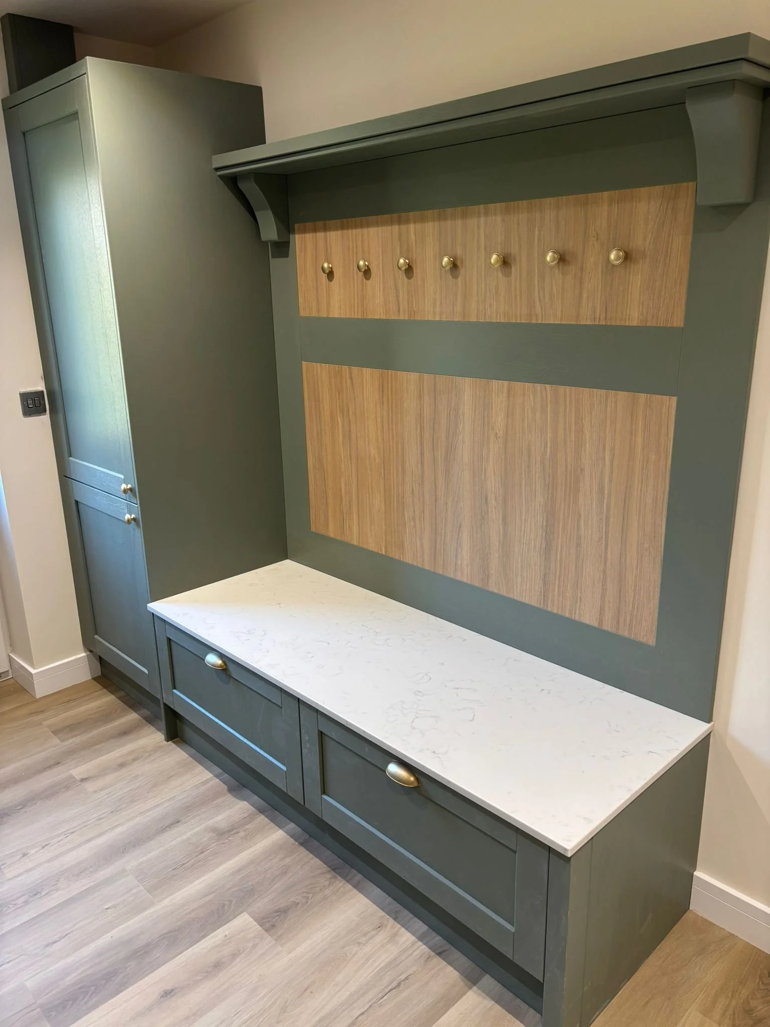 Interior of a modern entryway with a green storage cabinet, a white marble top bench, and a wall-mounted coat rack with six gold hooks.