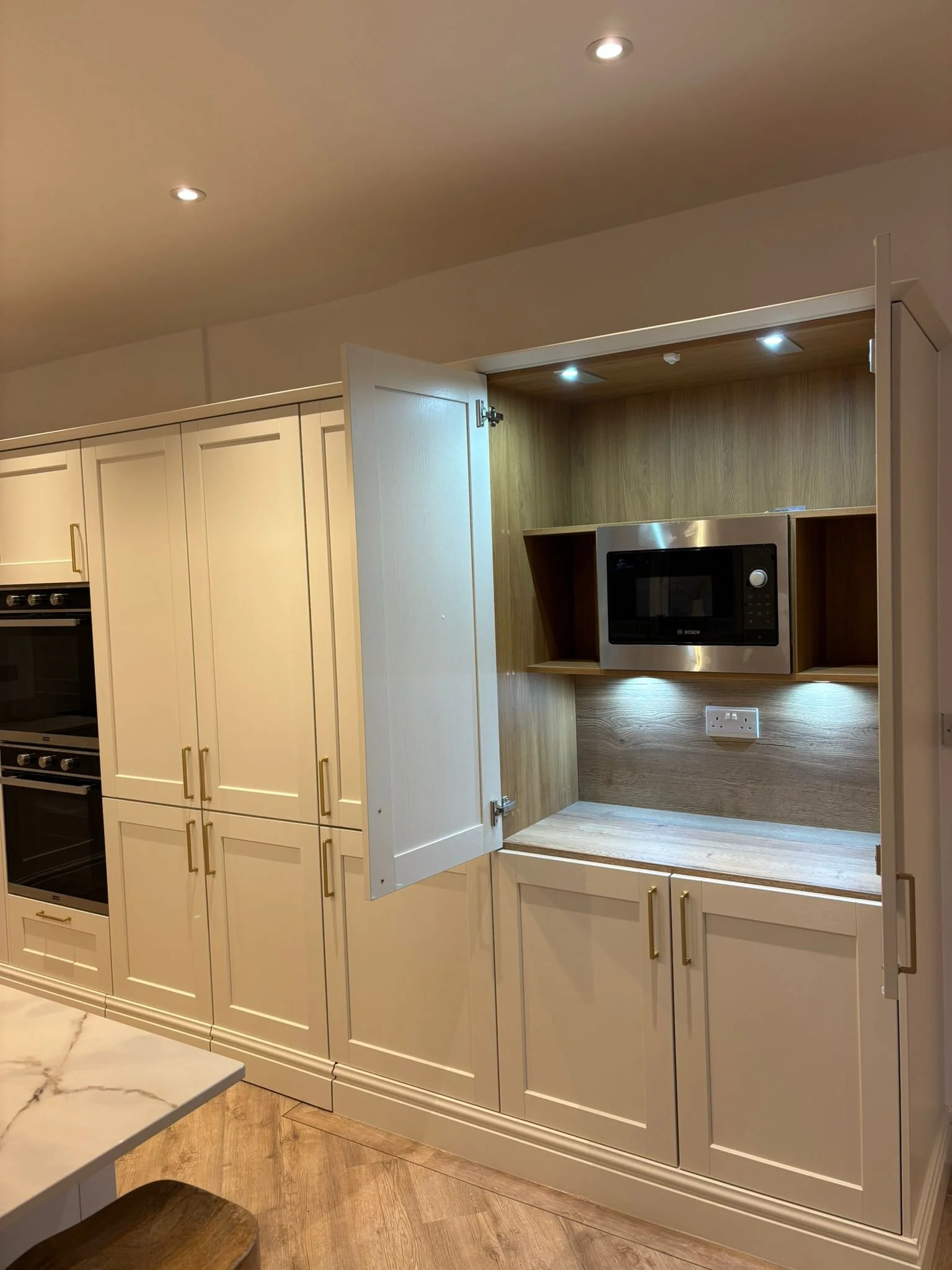 Kitchen with cream-colored cabinets, a built-in microwave, and wood countertop; open cabinet space with under-cabinet lighting.