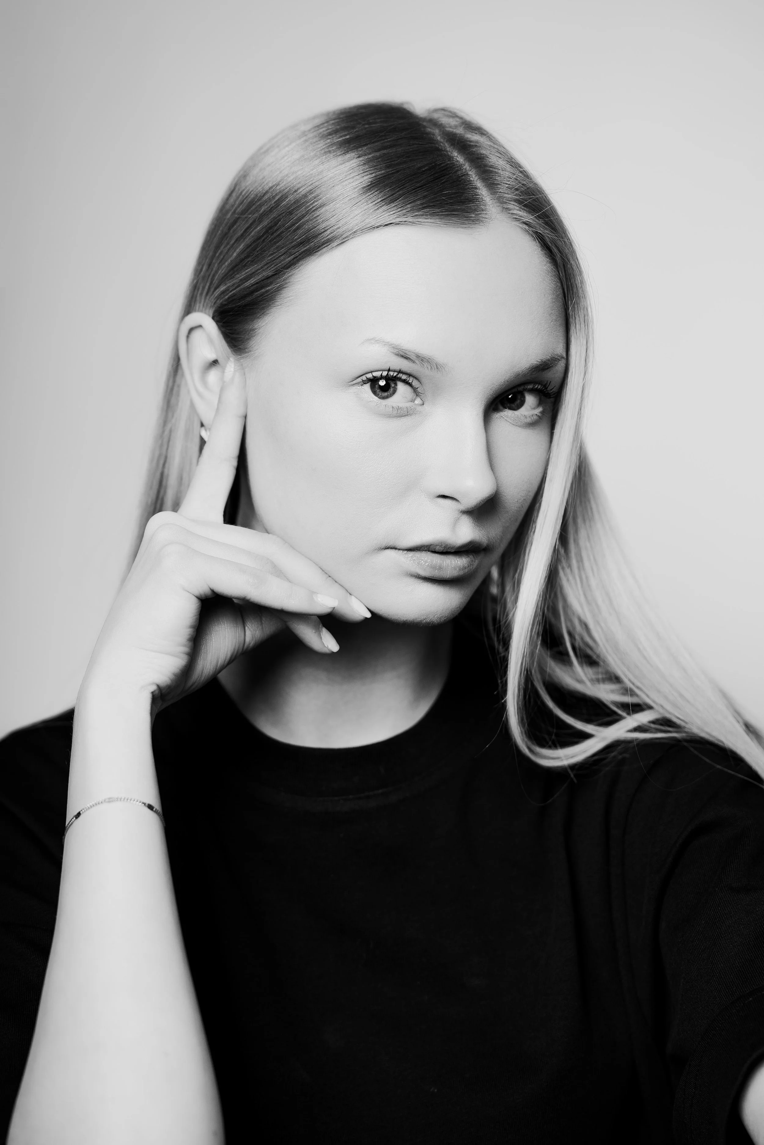 Black and white portrait of a young woman with straight hair, resting her chin on her hand, looking directly at the camera.