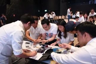 Group of young people gathered around a table, looking at documents or phones during a meeting or event.