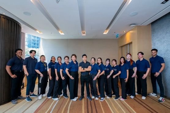 Group of 14 people in blue shirts standing indoors, posing for a photo.