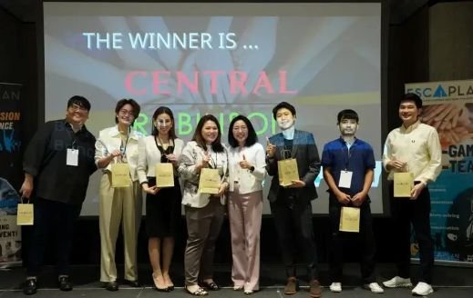 Group of eight people standing on stage holding awards, with a large screen behind them displaying the words 'The Winner Is... Central' and some text in the background.
