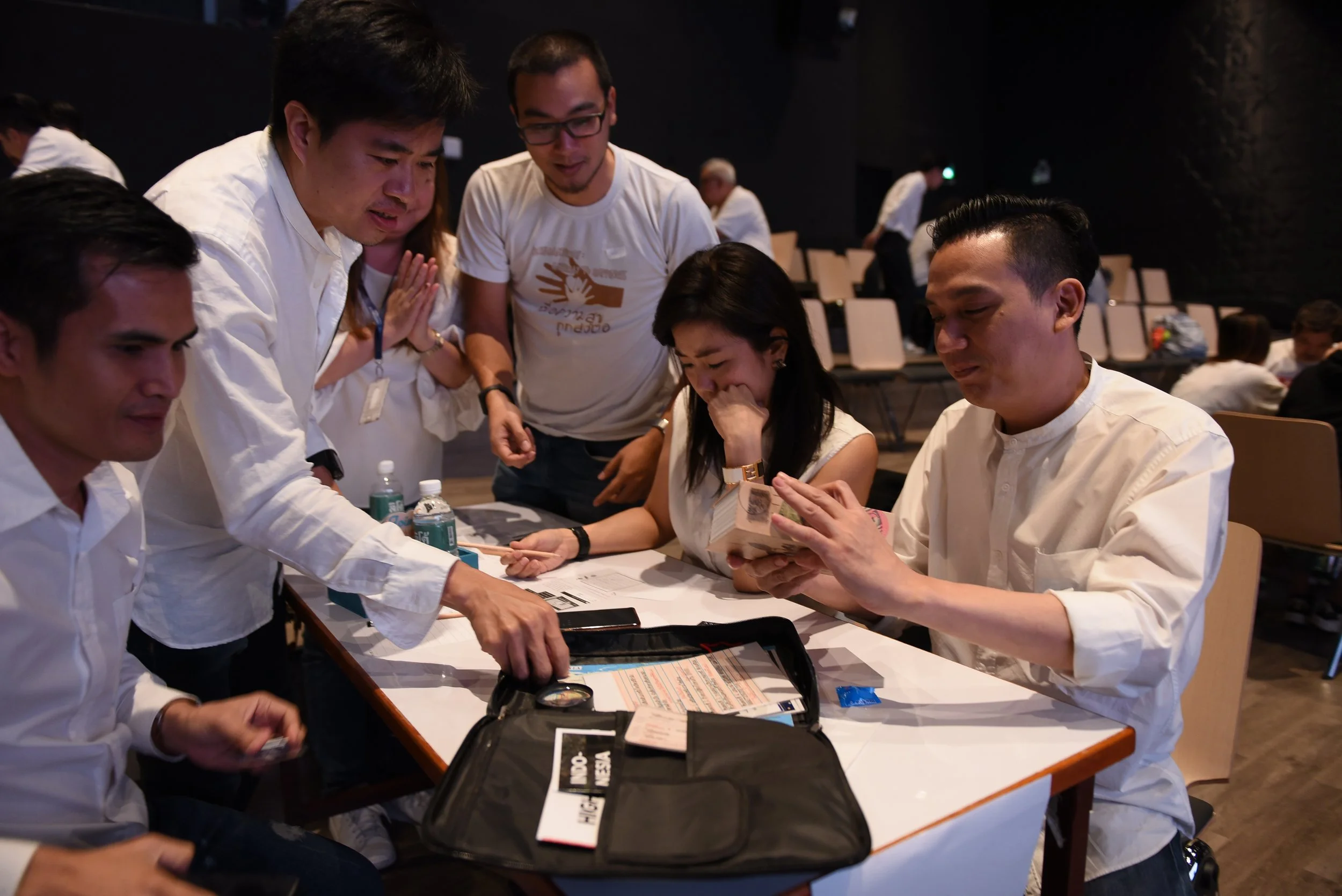 A group of people examining documents and money on a table during a meeting or workshop in a dimly lit room.