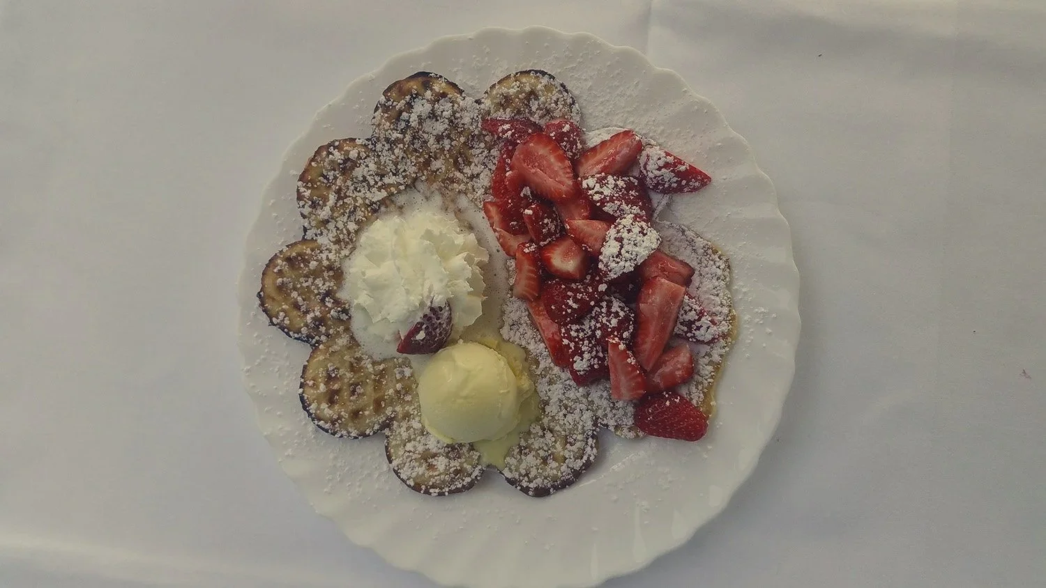 Ein Teller mit Waffeln, Erdbeeren und Bananen, garniert mit Puderzucker, Sahne und Vanilleeis.