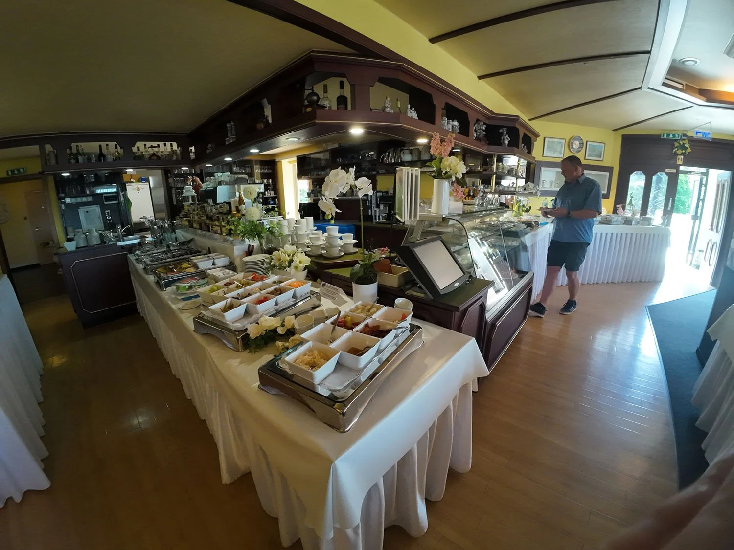 Ein Frühstücksbuffet im Themenhotel Bad Münder mit verschiedenen Speisen, Töpfen, Geschirr und Dekorationen, sowie einem Mann, der an einem Tisch steht.