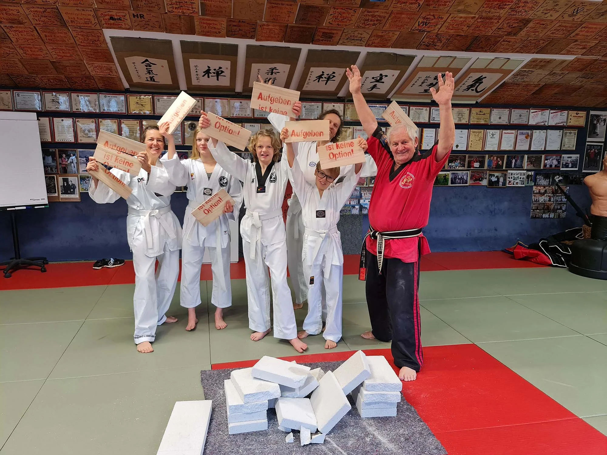 Menschen im Judo-Gi und einem Trainer in einem Dojo, die einen Schaumstoffblock zerstören, während sie protestieren, dass Aufgeben keine Option ist.
