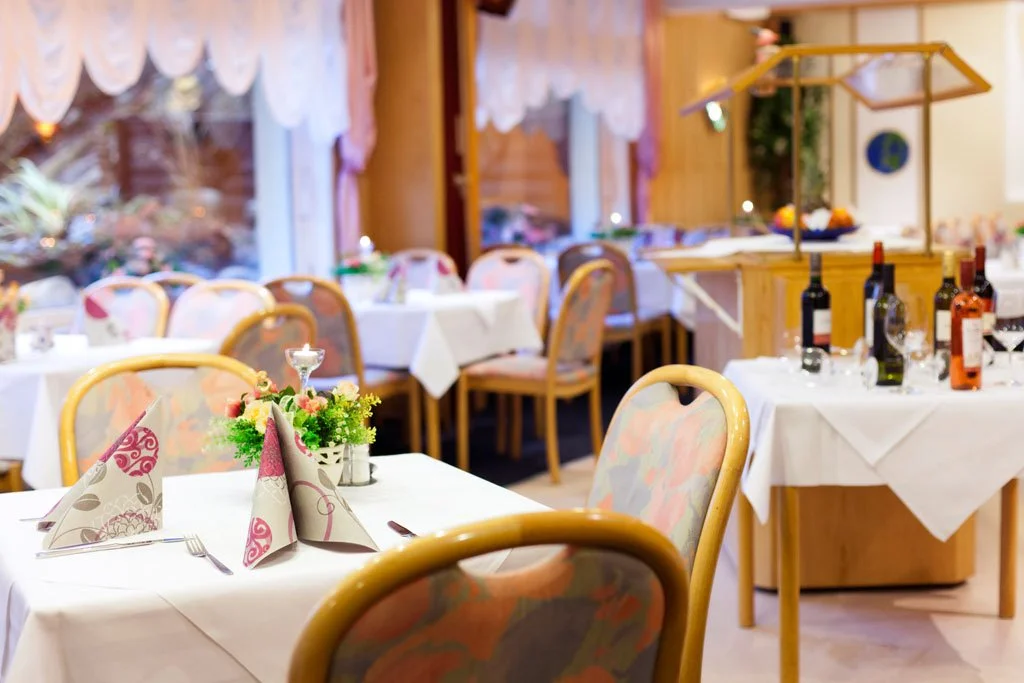 Ein eleganter Speiseraum mit gedeckten Tischen, Kerzen und Blumen, mit Wein- und Wasserflaschen, in einem stilvollen Restaurant oder Veranstaltungsraum.
