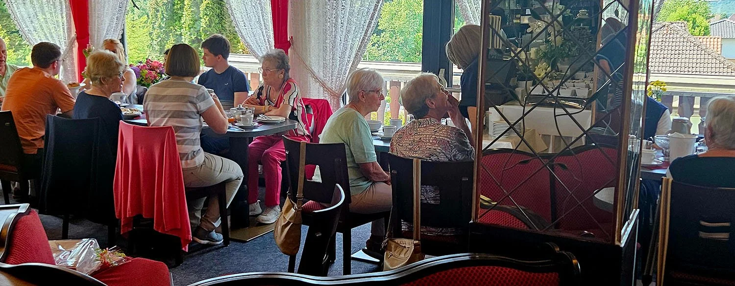 Mehrere Personen sitzen beim Frühstück im Hotel im Hotel Terrassen Cafe in Bad Münder. Es sind ältere und jüngere Menschen, die miteinander essen und trinken. 
